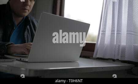 Porträt junger Mann auf dem Zug, druckt auf Laptop Stockfoto