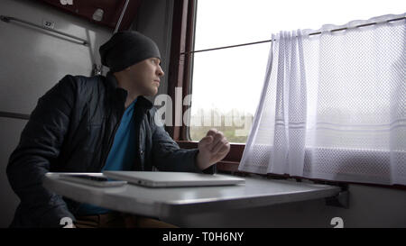 Junger Mann in einem Zug mit laotop, schaut aus dem Fenster Stockfoto