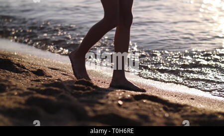 Junge ist zu Fuß entlang der goldenen Sand bei Sonnenuntergang am Strand, Füße close-up Stockfoto