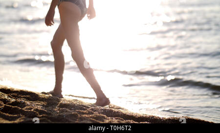 Junge ist zu Fuß entlang der goldenen Sand bei Sonnenuntergang am Strand, Füße close-up Stockfoto