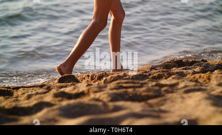 Junge ist zu Fuß entlang der goldenen Sand bei Sonnenuntergang am Strand, Füße close-up Stockfoto