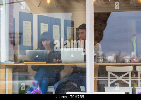 Junges Paar mit Apple Macs in einem Café zu einem Fenster sitzen, Großbritannien Stockfoto