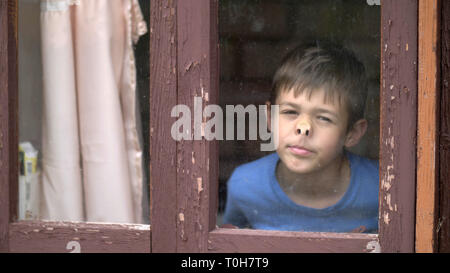 Lustig Junge lehnte sich Nase, um das Fenster zu Hause und blickt in die Kamera Stockfoto