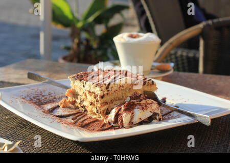 Seitliche Sicht auf frisch zubereitete Tiramisu mit Kakaopulver und choco Dressing, ein cappuchino Cup im Hintergrund. Eins für Zwei, Kuchen mit zwei Gabeln. Stockfoto