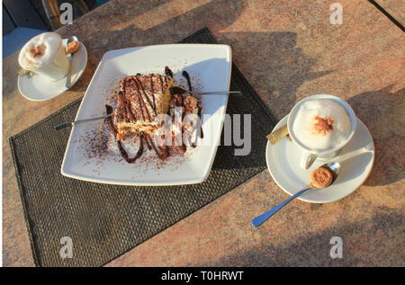 Frisch Tiramisu mit Kakaopulver und choco Abrichten auf eine Platte gemacht. Kuchen für Zwei, mit zwei Gabeln und zwei frische cappuchino Cups.. Stockfoto