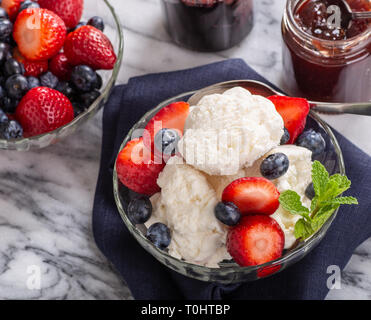 Glas Schale mit Vanilleeis mit Blaubeeren und Erdbeeren auf einem blau serviette Stockfoto