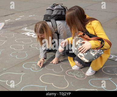 Zwei junge Frauen schreiben persönliche Nachrichten innerhalb von Herzen, auf dem Bürgersteig erstellt und eine Spende geben, auf dem Trafalgar Square, London, UK an einem sonnigen im März. Stockfoto