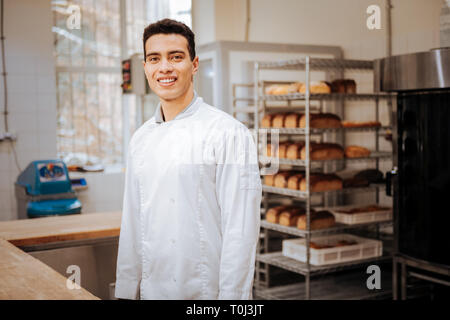 Junge dunkelhaarige Bäcker lächelnd während Gefühl vor Arbeit aufgeregt Stockfoto