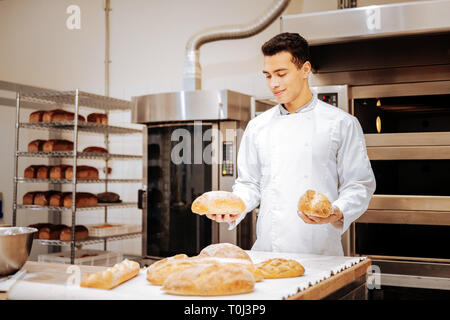 Dunkelhaarige zufrieden baker Holding zwei Laibe Brot in seine Hände Stockfoto