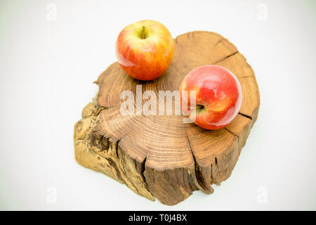 Zwei rote saftige Äpfel liegen auf einer hölzernen stumpf auf weißem Hintergrund. Frische Äpfel auf einer hölzernen anmelden. Lecker und reife Früchte. Gesunde Ernährung Konzept. Stockfoto