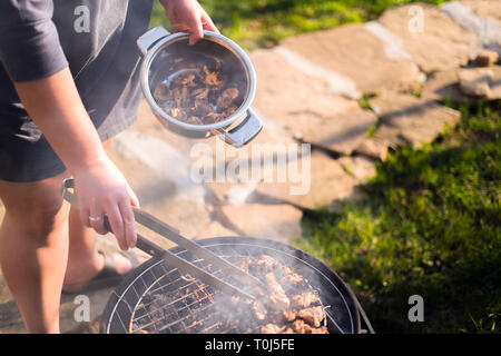 Frau Hände grillen Barbecue auf dem Grill im Freien im Hof treffen. Sommer Picknick. Braten Metallgitter auf heißen Kohlen. Rauchen fügt ein Stockfoto