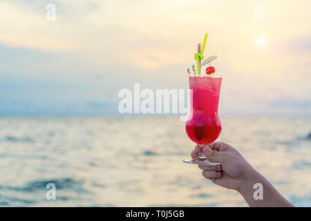 Hand red Cocktail in der Dämmerung das Meer und Himmel Hintergrund. Sommer, Ferien, Reisen und Urlaub. Stockfoto