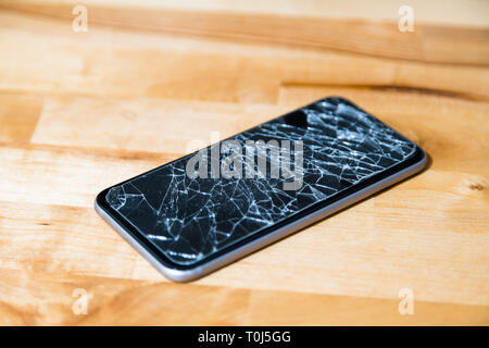 Konzept des smart phone mit defekten Bildschirm. Draufsicht auf hölzernen Schreibtisch Hintergrund. Risse, zerschmettert, LCD-Touchscreen auf modernen Handys. Gadget muss r Stockfoto