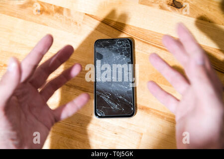 Konzept der fallenden smart phone mit defekten Bildschirm. Draufsicht auf hölzernen Schreibtisch Hintergrund. Risse, zerschmettert, LCD-Touchscreen auf modernen Handys. Gadget Stockfoto