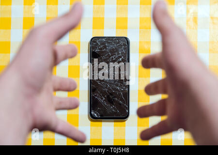 Konzept der fallenden smart phone mit defekten Bildschirm. Draufsicht auf gelb Schreibtisch Hintergrund. Risse, zerschmettert, LCD-Touchscreen auf modernen Handys. Gadget Stockfoto