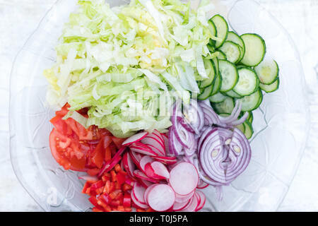 Blick von oben auf die frisch geschnittenen Sommer Salat. Viele köstliche Gemüse im Glas Salat - Gurke, Salat, Radieschen, Tomaten, roten Zwiebeln Stockfoto