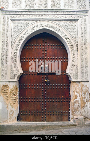 Eine hölzerne Tür in Hufeisenform gegen eine weiße Wand, reich mit typisch islamisches geometrischen Mustern verziert; beschmutzt in Fes (Marokko). Stockfoto