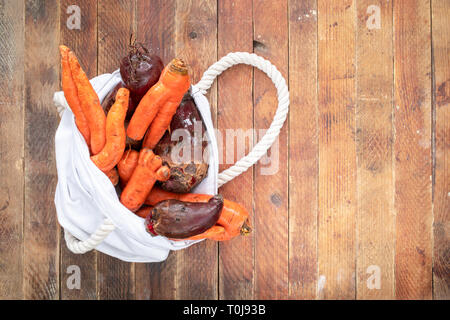 Beutel mit weißer Bettwäsche gewaschen nicht-standard hässlich Gemüse auf Holztisch. Stockfoto