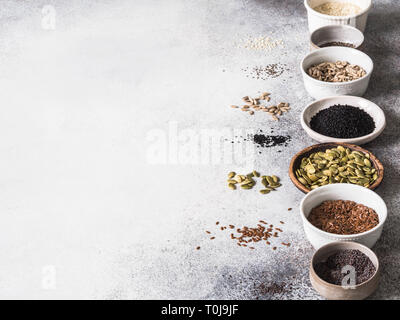 Verschiedene Samen - Sesam, Leinsamen, Sonnenblumenkerne, Kürbiskerne, Mohn, Chia in Schalen auf grauem Hintergrund. Stockfoto