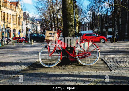 Rotes Fahrrad unter einem Baum vor der roten Autos gesperrt. Utrecht, Holland. Stockfoto