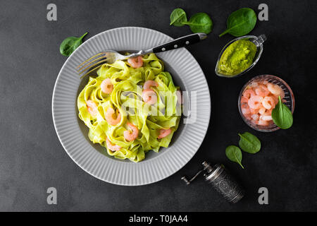 Gekochte Fettuccine Pasta mit frischen Spinat Pesto und Garnelen auf schwarzem Hintergrund. Italienische Küche. Gesundes Gericht für das Mittagessen. Ansicht von oben Stockfoto