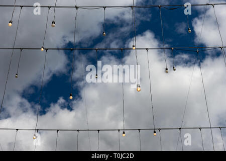 Beleuchteten Glühbirnen hängen von schwarzen Kabel vor dem Hintergrund des tief blauen Himmel und weiße und graue Wolken Stockfoto