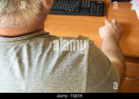 Ein älterer grauhaariger Mann nutzt einen Computer Maus, Arbeit zu Hause für Menschen mit Behinderung, Ausbildung Rentner auf einem PC zu arbeiten, ein Blick auf die Rückseite. Stockfoto