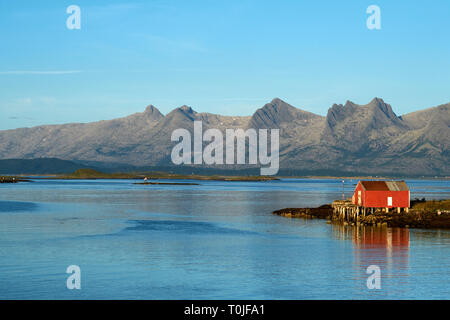 Eine rote Rorbuer in Haus und Küstenlinie und De Syv Søstre/die Sieben Schwestern Bergkette auf der Insel Alsten in Alstahaug in Nordland County, Norwegen Stockfoto