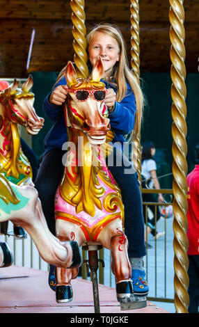 Ein junges Mädchen ein Pferd reiten auf einem traditionellen Jahrmarkt, ihre Sonnenbrille Holding über den Kopf des Pferdes Stockfoto