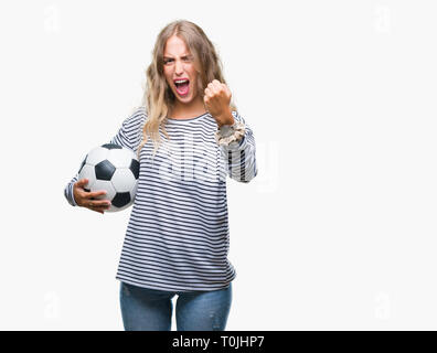 Schöne, junge blonde Frau mit Fußball-Fußball-Kugel über isolierte Hintergrund genervt und frustriert schrie mit Zorn, verrückt und mit Schreien Stockfoto