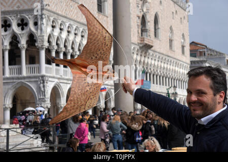 Venedig, Italien. 20 Mär, 2019. Ein Kellner an der Todaro Cafe, in dem San Marco Platz, zeigt die Hawk-förmiger Drachen, der sich über die Tische im Freien fliegen die Möwen am 20. März, 2019 in Venedig, Italien zu erschrecken. Hungriger Möwen zögern Sie nicht Touristen, Sandwiches oder Vorspeisen zu stehlen, um anzugreifen, während Sie ein Getränk an den Tischen der Cafés von San Marco Platz gesessen haben. Quelle: Andrea Merola/Erwachen/Alamy leben Nachrichten Stockfoto