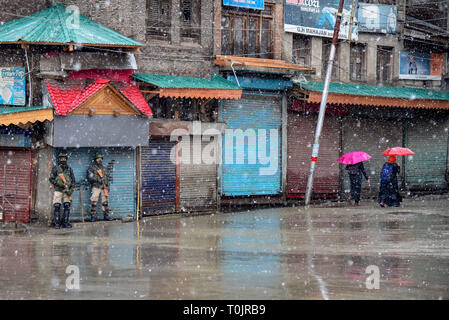 Srinagar, Jammu und Kaschmir, Indien. 20 Mär, 2019. Kaschmir Frauen gesehen vorbei Indischen paramilitärischen stehende Männer auf der Hut inmitten Schneefall in einer Sicherheitsabschaltung in Srinagar. Leben waren in Kaschmir Valley am Mittwoch aufgrund eines Protestes Abschaltung durch die Separatisten gegen die Freiheitsentziehenden Tod einer Lehrerin gestern als betroffen. Kräfte in ausreichender Anzahl waren auch in sensiblen Bereichen eingesetzt Die protestaktionen im Hinblick auf die Abschaltung Anruf vom seperatists zu vereiteln. Kredit Idrees: Abbas/SOPA Images/ZUMA Draht/Alamy leben Nachrichten Stockfoto