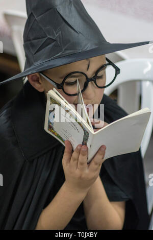 Elkana, Israel. 20 Mär, 2019. Ein Junge, gekleidet wie ein sorcered, liest das Buch Esther in der Synagoge in der israelischen Ortschaft Elkana während der jüdische Feiertag Purim. In diesem Urlaub Juden traditionell verkleiden sich, lesen Sie das Buch von Esther, eine Geschichte über ein anti-jüdischen fehlgeschlagen Grundstück im alten Persien, und, wann immer ein Schläger der Name Haman, der main Antagonist, erwähnt wird. Credit: Yagil Henkin/Alamy leben Nachrichten Stockfoto