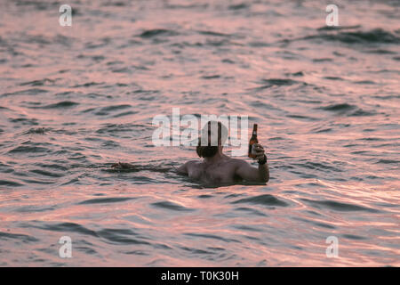 Adelaide, Australien. 21 Mär, 2019. Schwimmer im Wasser des Ozeans, die ein Toast mit Bierflaschen, wie die Sonne über Grange Strand in Adelaide Credit Sets: Amer ghazzal/Alamy leben Nachrichten Stockfoto