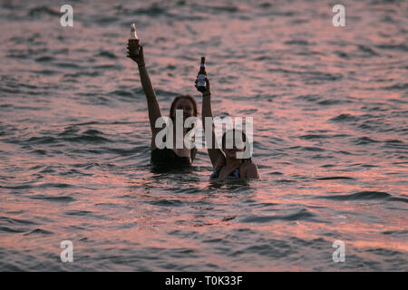 Adelaide, Australien. 21 Mär, 2019. Schwimmer im Wasser des Ozeans, die ein Toast mit Bierflaschen, wie die Sonne über Grange Strand in Adelaide Credit Sets: Amer ghazzal/Alamy leben Nachrichten Stockfoto