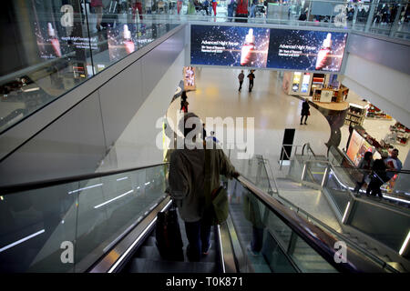 England Heathrow Airport Terminal 2 Passagier auf Rolltreppe mit Koffer in Richtung Abflughalle Stockfoto