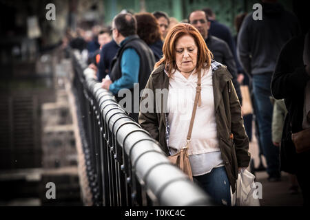 Frau in einer Menschenmenge schaut und geht über die Brücke, mit traurigen/besorgt/nachdenklich/einsame Blick auf ihrem Gesicht. Stockfoto