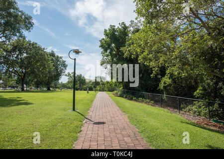 Brick Bürgersteig und üppigem Grün an Bicentennial Park unter einem blauen Himmel mit Wolken in Darwin, Australien Stockfoto