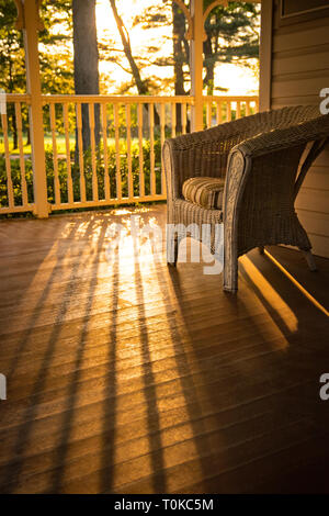 Warme, sonnige Aussicht von zu Hause: einen Korbstuhl auf hölzernen Veranda. Stockfoto