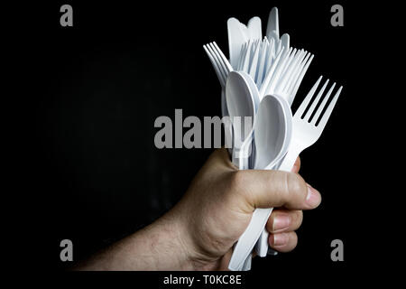 Einwegflaschen aus Plastik Besteck in einem Bündel; in der Hand auf dunklem Hintergrund. Stockfoto