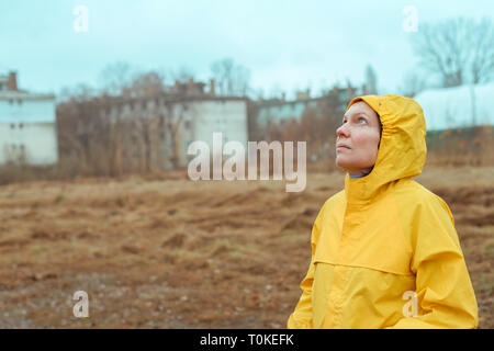Frau im gelben Regenmantel zu regnerischen Wolken, während die Regentropfen fallen auf ihrem Gesicht sind Stockfoto