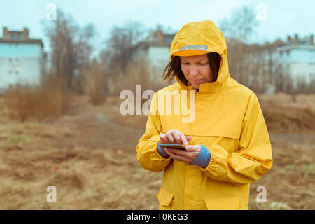 Frau im gelben Regenmantel SMS auf Handy im Freien an regnerischen Tag Stockfoto