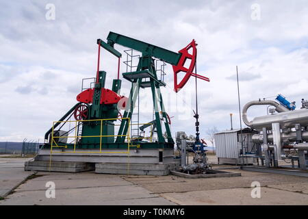 Grüne und rote Pferd pumpjack, Öl, Öl derrick Öl gut Pumpen mit dramatischen bewölkter Himmel Hintergrund Stockfoto