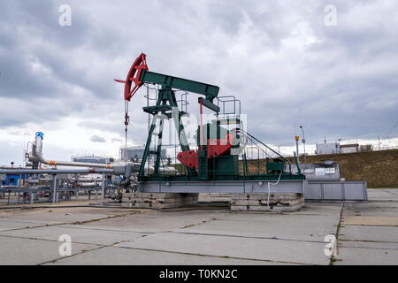 Grüne und rote Pferd pumpjack, Öl, Öl derrick Öl gut Pumpen mit dramatischen bewölkter Himmel Hintergrund Stockfoto