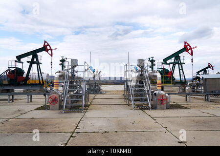 Grüne und rote Pferd pumpjack, Öl, Öl derrick Öl gut Pumpen mit dramatischen bewölkter Himmel Hintergrund Stockfoto