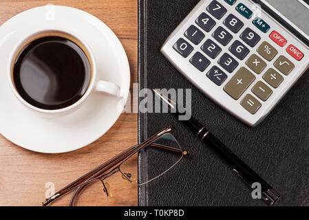 Tasse Kaffee, Notebook, Gläser, Taschenrechner und Kugelschreiber auf hölzernen Hintergrund Stockfoto