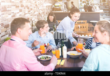 Höflich charmante Kellnerin Gerichte zu Familie im Cafe mit Stockfoto