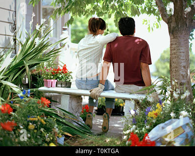 Ansicht der Rückseite des jungen Paares nebeneinander sitzen auf der Gartenbank. Stockfoto