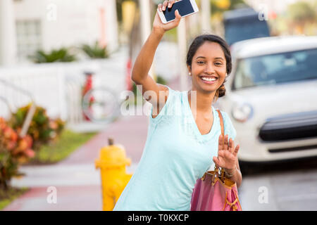 Junge Frau mit ihrem Telefon ihre Hand winken für Ihre Fahrt Stockfoto