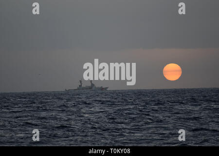 Der U.S. Coast Guard Cutter Mellon (WHEC717) die Besatzung und eine Air Station Herrenfriseure Punkt MH-65 Dolphin Hubschrauberbesatzung Recherchen kurz vor Sonnenuntergang 24 Meilen südlich von Oahu, 18. März 2019. Die Mannschaften haben nach über 2300 km2, da die Suche März 17, 2019 begonnen. (U.S. Coast Guard Foto von Lt. j.g. Joshua Martin/Freigegeben) Stockfoto